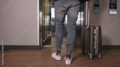 Black businessman walking to elevator and pushing lift button down on panel in apartment corridor. Close up black man entering into elevator car and door closing