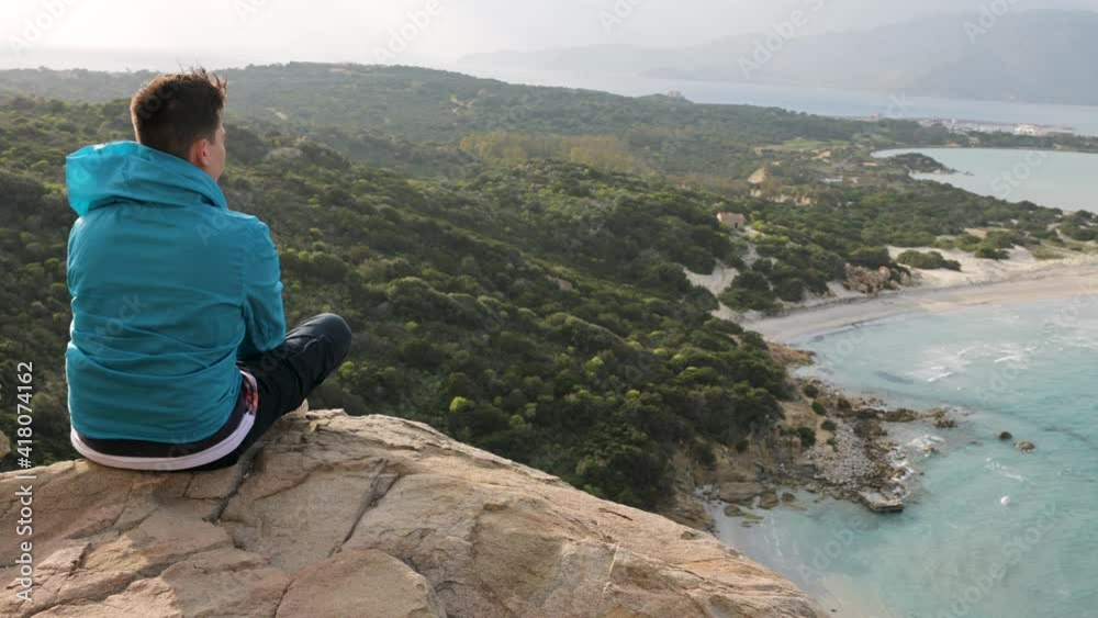Unrecognizable young man sitting on a cliff looking at the beautiful panorama on translucent sea. Breath of Fresh Air concept Unrecognizable young man sitting on a cliff looking at the beautiful panorama on translucent sea. Breath of Fresh Air concept
