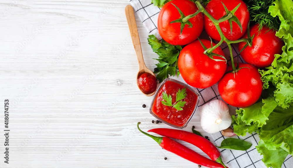 Sauce or ketchup and ingredients for his cooking: tomatoes, garlic, basil, parsley, red hot pepper and spices on a wooden white background. Close-up. Top view. Place for text. Sauce or ketchup and ingredients for his cooking: tomatoes, garlic, basil, parsley, red hot pepper and spices on a wooden white background. Close-up. Top view. Place for text.