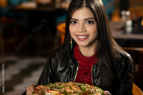 Portrait of a beautiful young Indian girl eating food while sitting in a restaurant.