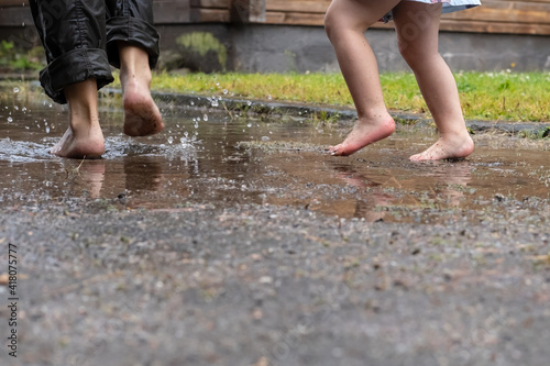 Mother and child are having fun running through the puddles, after the rain in the yard of their house. Lifestyle.  © koldunova