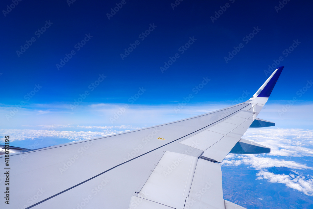 Photo of airplane wing with clouds background, horizon line and clear blue sky