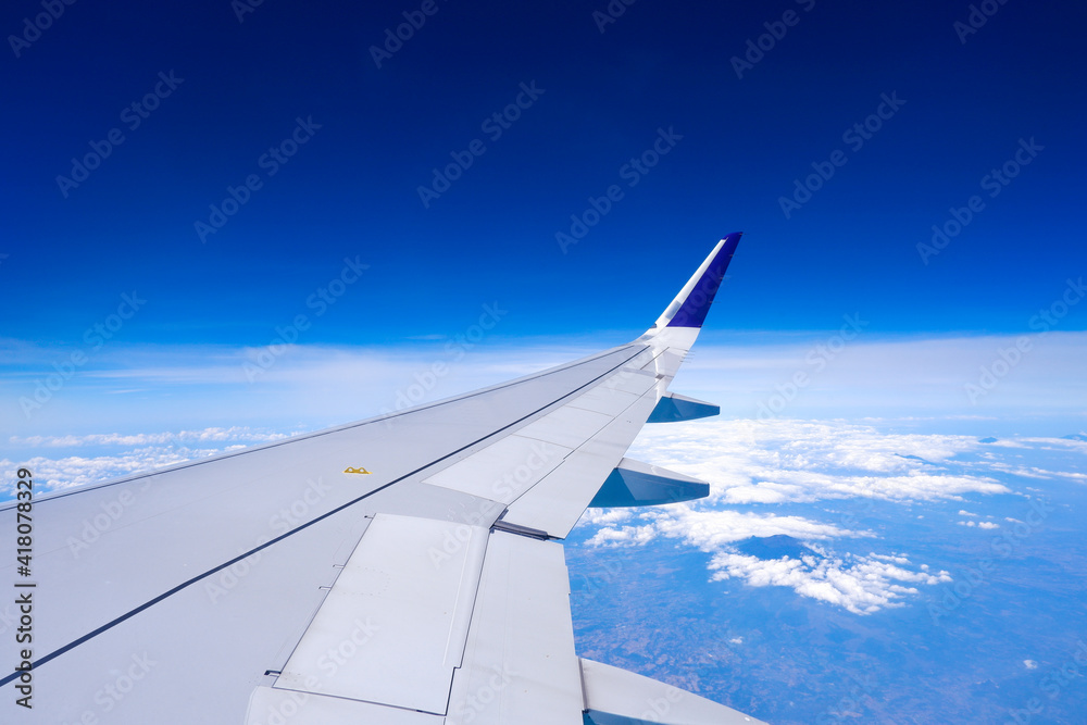 Photo of airplane wing with clouds background, horizon line and clear blue sky