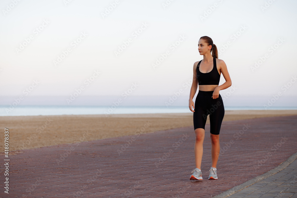 girl runner in a black tracksuit and sneakers runs by the sea during sunset girl runner in a black tracksuit and sneakers runs by the sea during sunset