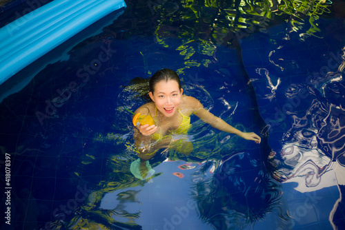 beautiful Asian woman enjoying luxury holidays trip - young attractive and happy Chinese girl in bikini relaxed at tropical villa resort drinking orange cocktail in swimming pool