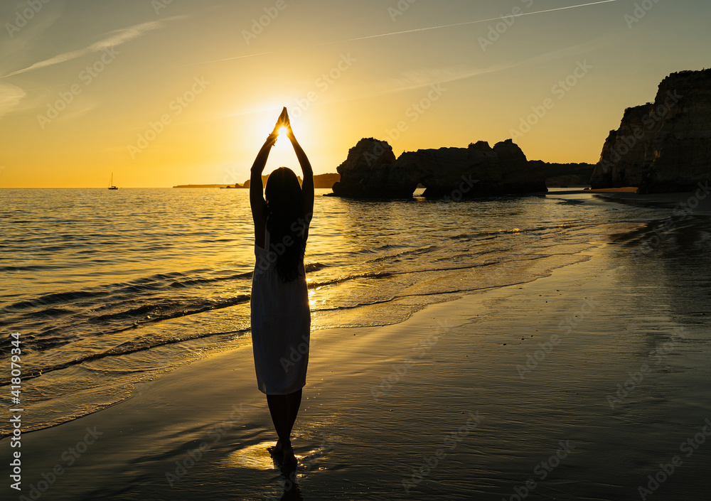 Woman making shilouette with hands and the sun at sunset in the beach