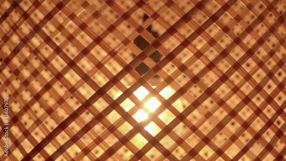 A bamboo wooden lamp shade with an electric light bulb rotates in the room. Artificial lighting effect, interior and bamboo lamp design concept. A bamboo wooden lamp shade with an electric light bulb rotates in the room. Artificial lighting effect, interior and bamboo lamp design concept.