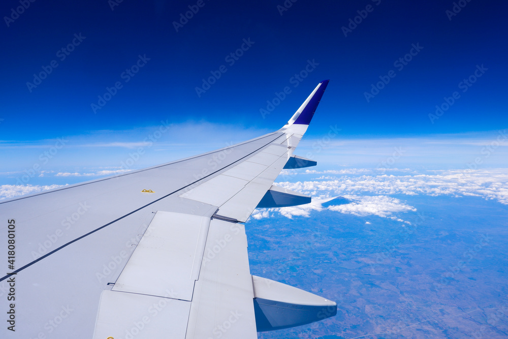 Photo of airplane wing with clouds background, horizon line and clear blue sky