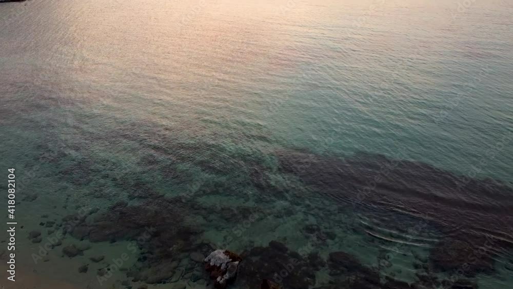 Aerial view of a calm translucent blue water sea during sunset. Drone flying over waters. Aerial view of a calm translucent blue water sea during sunset. Drone flying over waters.