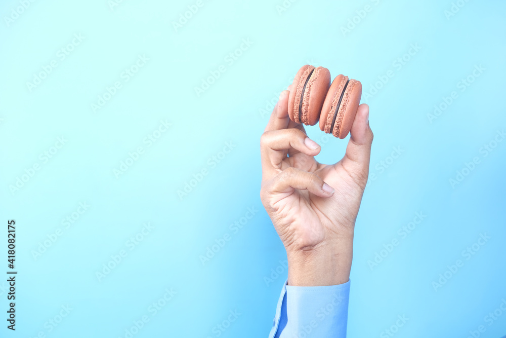 Fototapeta premium hand holding chocolate macaroon against blue background 