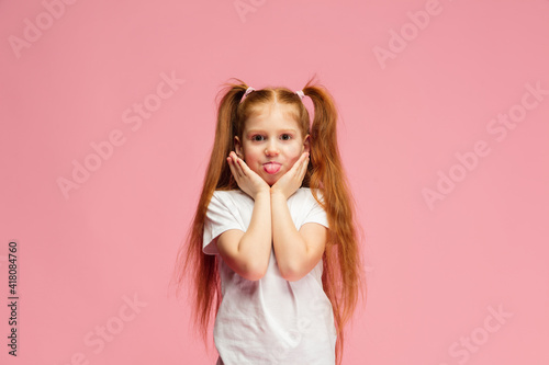 Sticking out tongue. Happy, smiley little caucasian girl isolated on pink background with copyspace for ad. Looks happy, cheerful. Childhood, education, human emotions, facial expression concept.