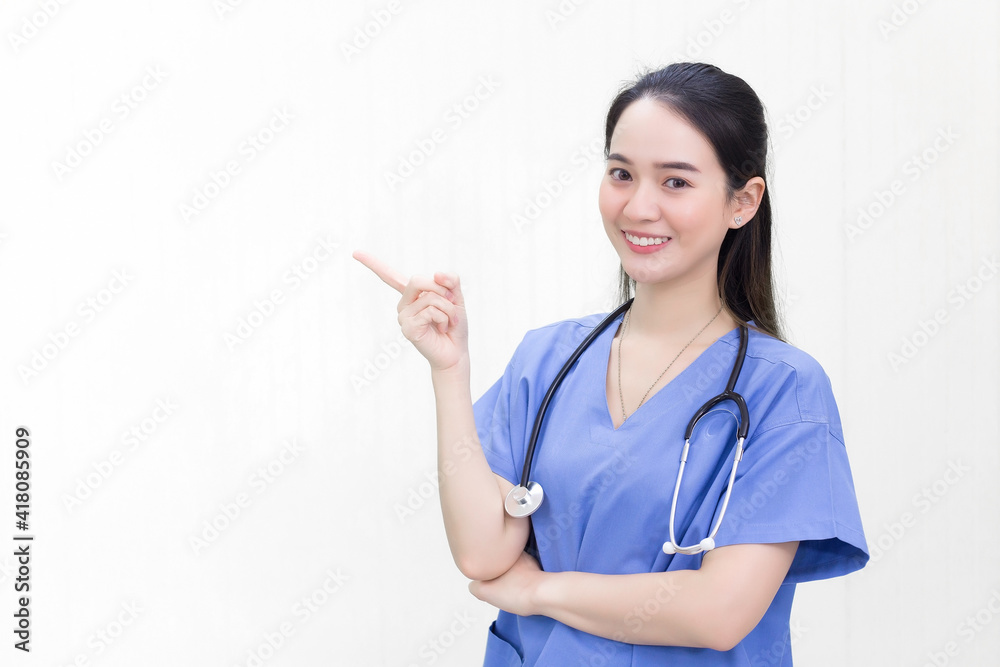 A beautiful young Asian woman doctor in a blue uniform stands and smiles while pointing to the top on a white background. A beautiful young Asian woman doctor in a blue uniform stands and smiles while pointing to the top on a white background.