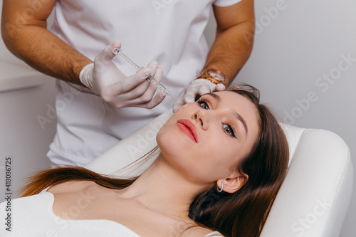Young brunette woman receiving plastic surgery injection on her face, closeup portrait