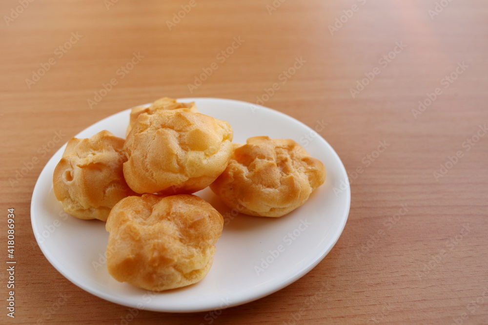 Round shape choux cream group on round white dish and light brown wood background. Round shape choux cream group on round white dish and light brown wood background.