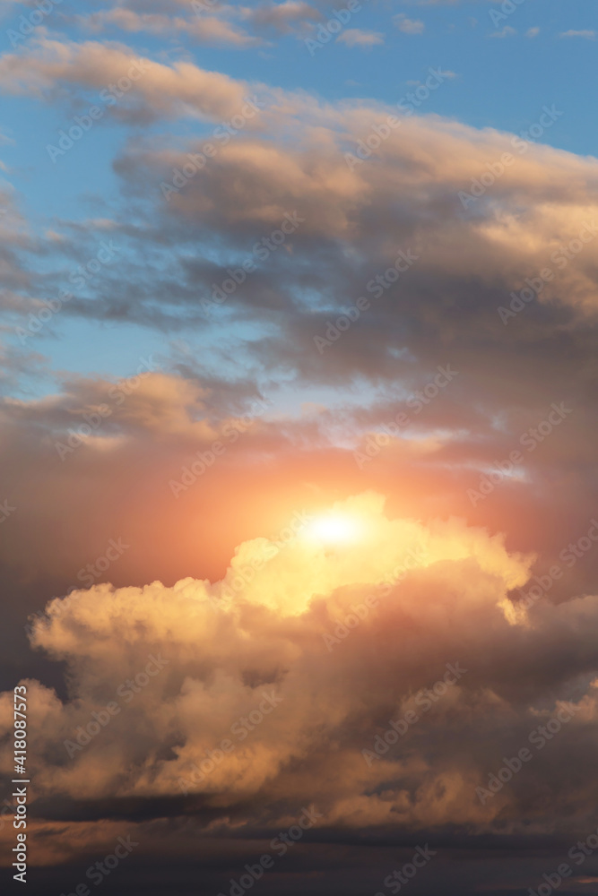 Epic sunset storm sky with sun and yellow orange sunlight. Big dark fluffy cumulus clouds on blue sky background texture