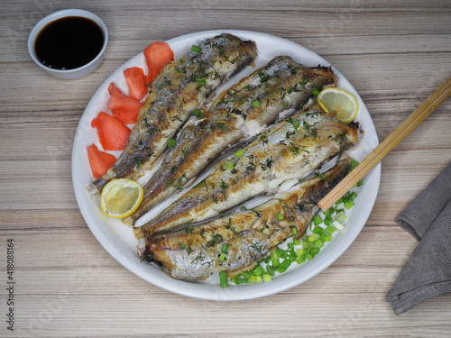 Fried fish micromesistius poutassou with lemon, pickled ginger in a plate, soy sauce and chopsticks on the table, flat layout. Healthy seafood for dietary nutrition, delicious light snack for beer photo