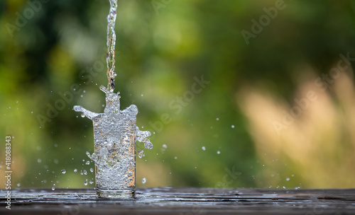 Drink water pouring in to glass over sunlight and natural green background.Water splash in glass Select focus blurred background