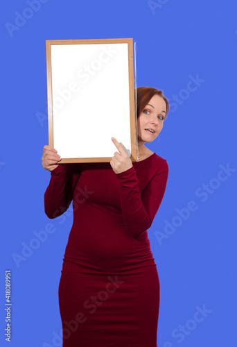woman in red dress points finger at blank board on blue background