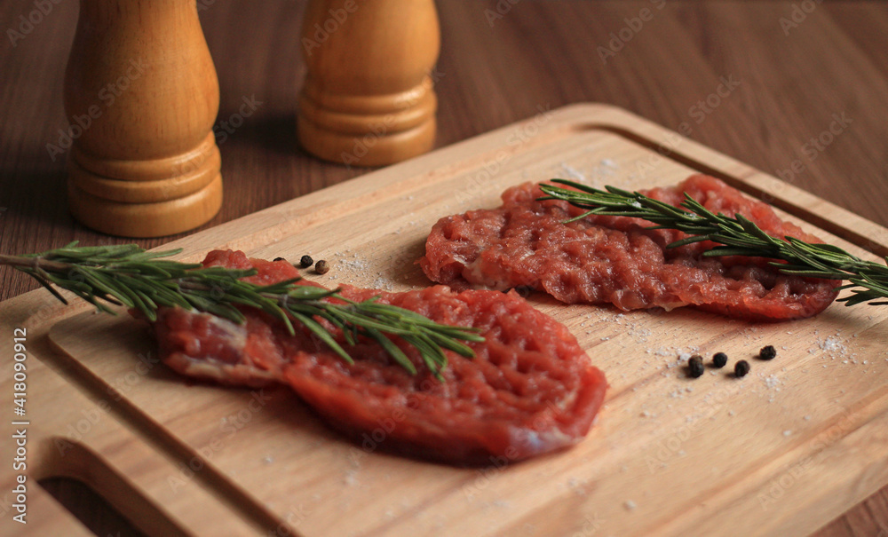 raw piece of pork chop with seasonings and a sprig of rosemary on a wooden board
