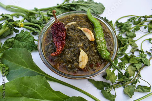 Indian homemade curry Sarson ka saag ki sabji served in transparent bowl garnished with fried green chilly, red chilly and garlic cloves. Authentic North indian Punjabi sabzi. Decorated with raw leaf photo