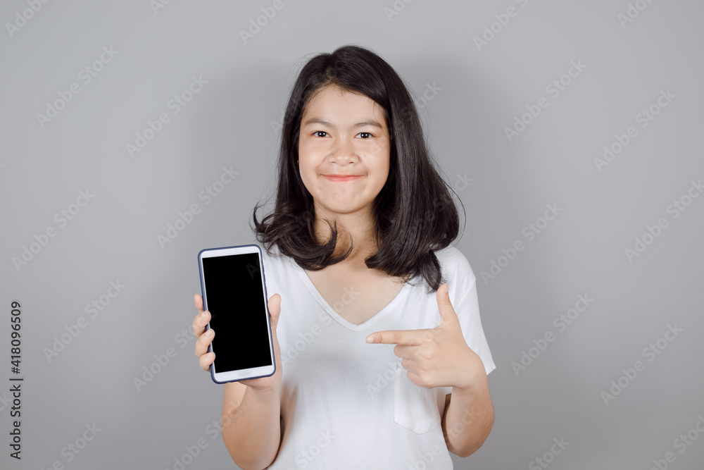 Portrait of smiling Asian teenager wears white t-shirt showing blank screen mobile phone or smart phone isolated on gray background, Mock up copy space Portrait of smiling Asian teenager wears white t-shirt showing blank screen mobile phone or smart phone isolated on gray background, Mock up copy space