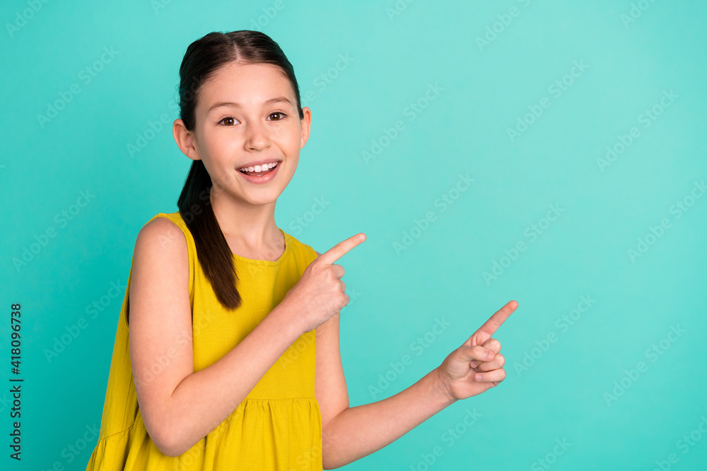 Photo of optimistic nice brown hair girl point empty space wear yellow dress isolated on bright teal color background Photo of optimistic nice brown hair girl point empty space wear yellow dress isolated on bright teal color background
