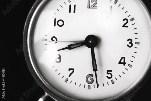 A black-and-white image of the dial of an old clock that shows half past eight in the morning. The clock stands on a dark background. The transience of time. The fading past.