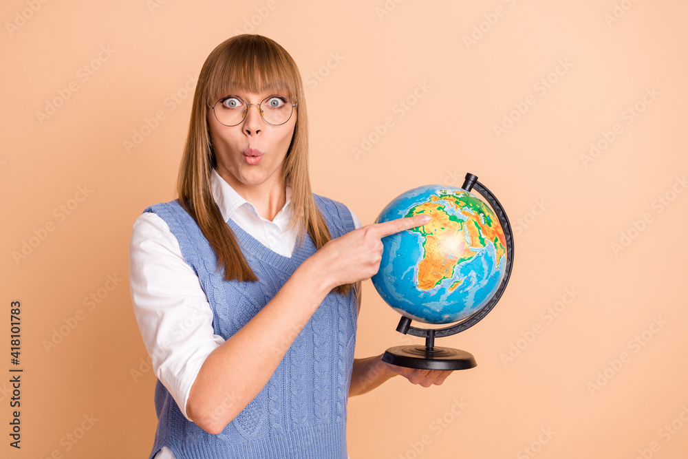 Photo portrait of amazed girl pointing at continent on globe at school isolated on pastel beige color background Photo portrait of amazed girl pointing at continent on globe at school isolated on pastel beige color background