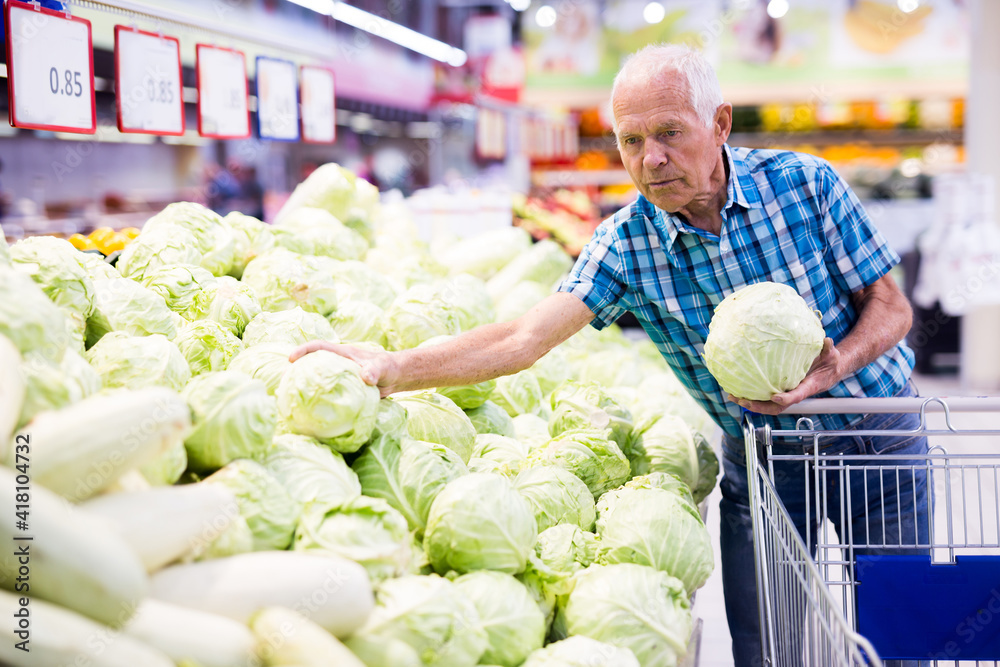 Fototapeta premium Elderly retired man buying cabbages in grocery department of the supermarket