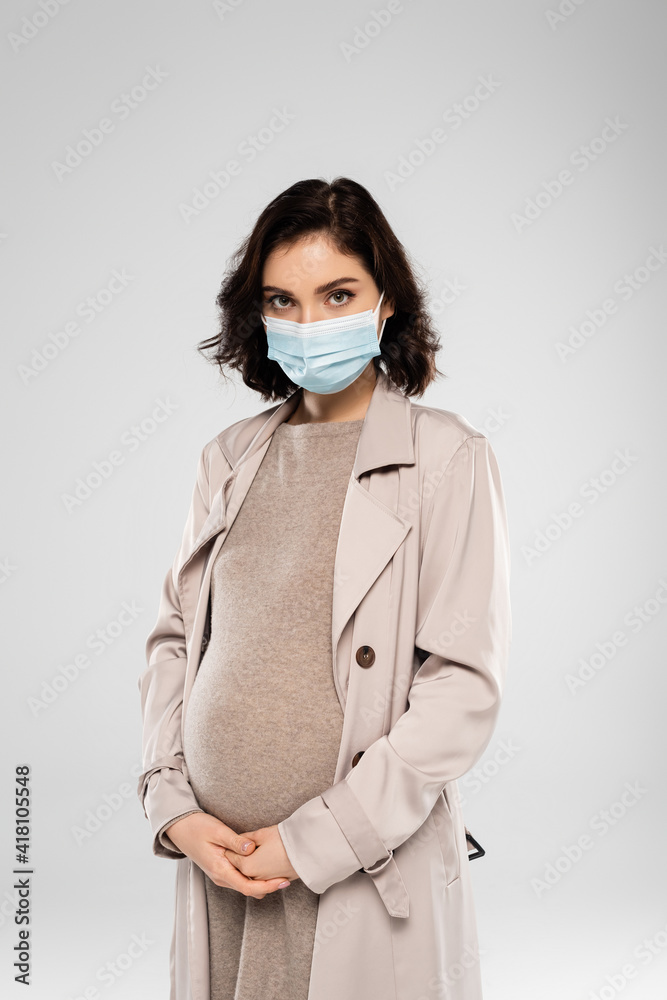 Young pregnant woman in medical mask looking at camera isolated on grey Young pregnant woman in medical mask looking at camera isolated on grey