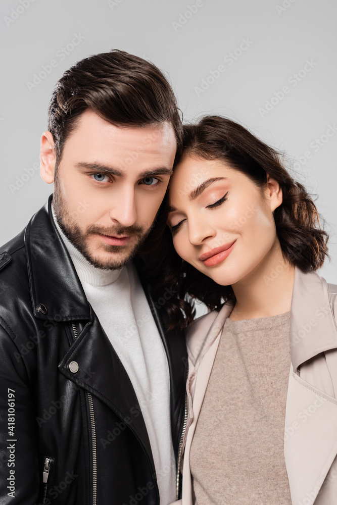 Man in leather jacket looking at camera near brunette wife isolated on grey Man in leather jacket looking at camera near brunette wife isolated on grey