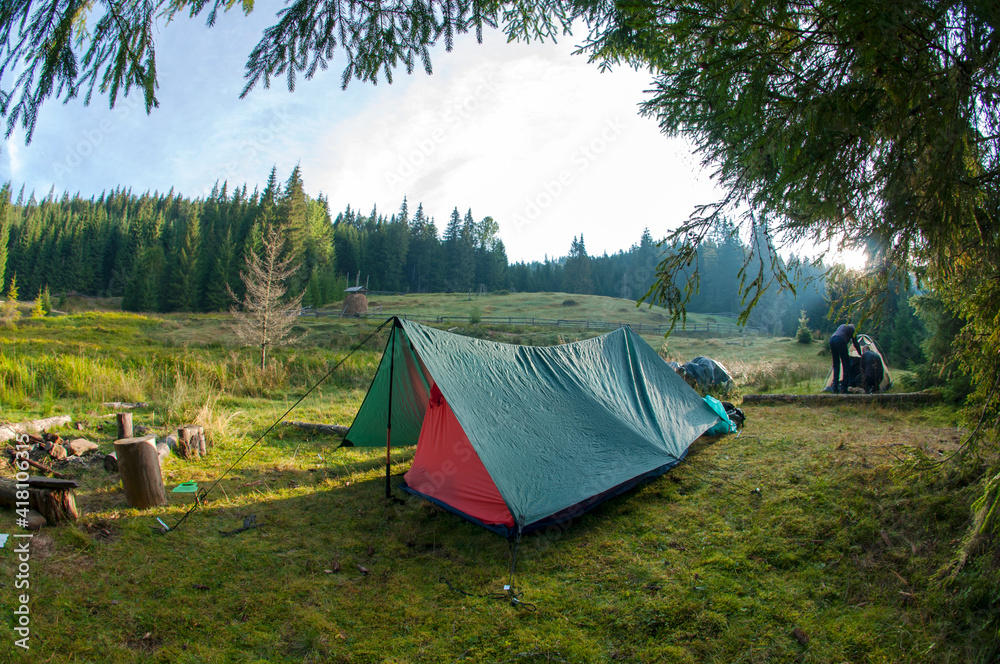 tourist tent stands on a green meadow against the backdrop of forests and peaks