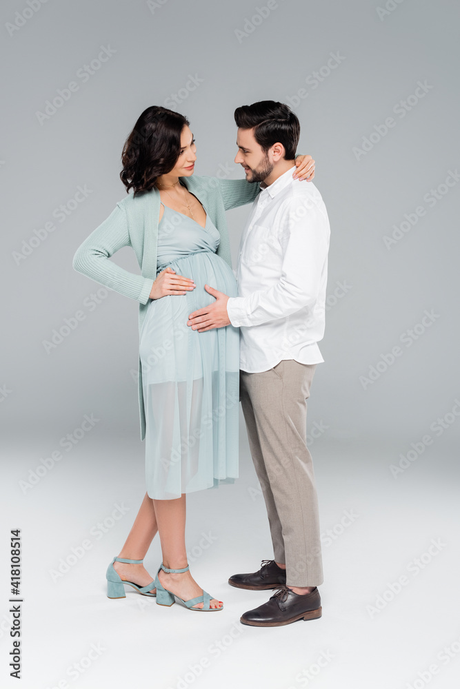 Stylish pregnant woman hugging husband on grey background Stylish pregnant woman hugging husband on grey background