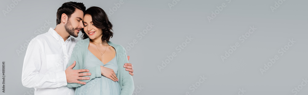 Young man hugging pregnant wife isolated on grey, banner Young man hugging pregnant wife isolated on grey, banner