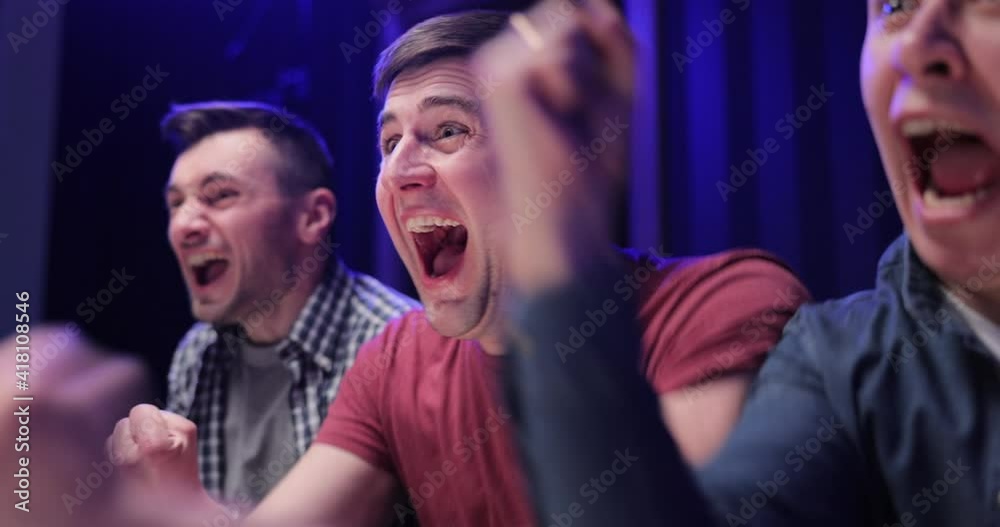 Close up of Caucasian male football fan sitting with friends at TV screen in dark living room and watching match. Cheerful man celebrating football win. Scoring goal or winning game concept Close up of Caucasian male football fan sitting with friends at TV screen in dark living room and watching match. Cheerful man celebrating football win. Scoring goal or winning game concept