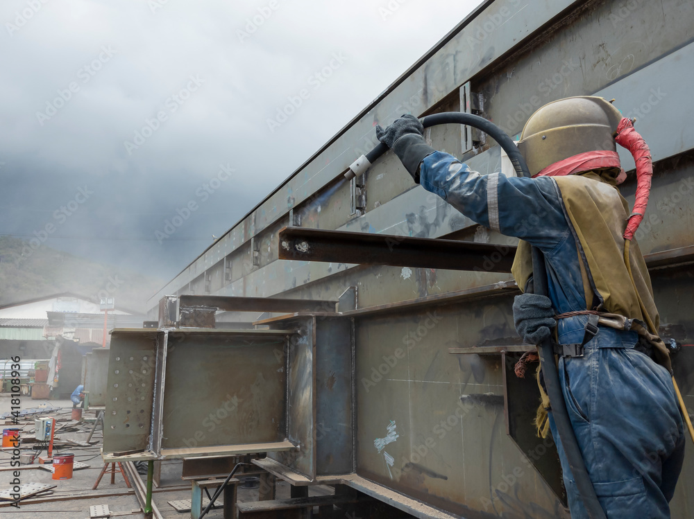 Worker is sandblasting a welding surface and steel structure with pressure blasting pot for create surface profile of steel before painting. Worker is sandblasting a welding surface and steel structure with pressure blasting pot for create surface profile of steel before painting.
