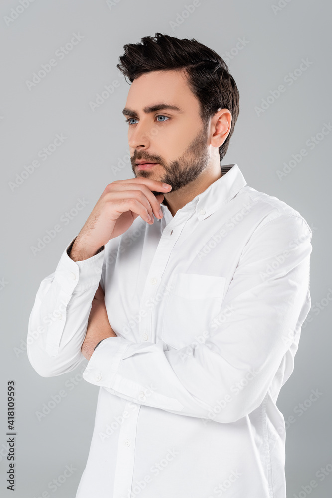 Young man in white shirt holding hand near chin isolated on grey Young man in white shirt holding hand near chin isolated on grey