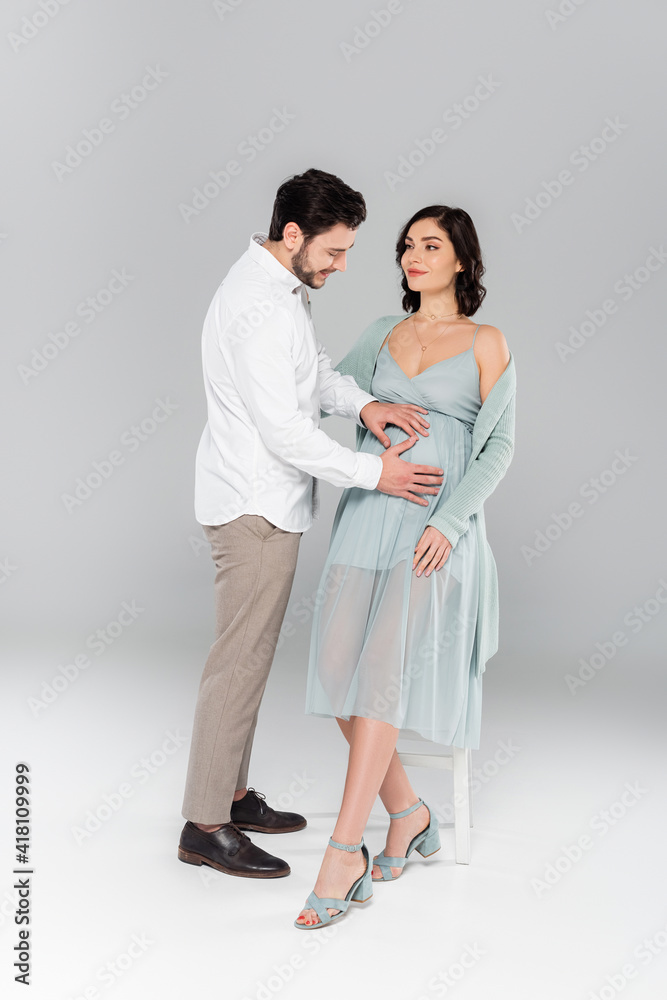 Cheerful man holding hands on belly of pregnant wife on grey background Cheerful man holding hands on belly of pregnant wife on grey background