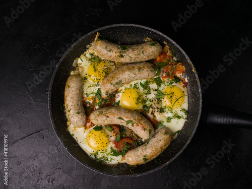 Pan-fried sausages and eggs. View from above. Studio photo on black background