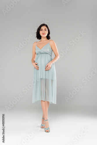 Pretty pregnant woman in dress looking at camera on grey background