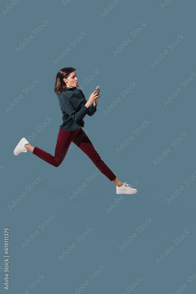 Scrolling phone on the run. High angle view of young woman on blue studio background. Human emotions and facial expressions concept. Full length portait, copyspace for ad. Fashion, retro style. Scrolling phone on the run. High angle view of young woman on blue studio background. Human emotions and facial expressions concept. Full length portait, copyspace for ad. Fashion, retro style.