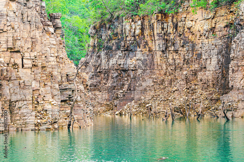 Beautiful landscape with sedimentary rock walls and some dry tree branches out of the water of the lake. Photo at Lake of Furnas, Capitólio MG, Brazil.