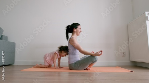 Pretty baby girl playing with her mom while she is doing yoga at home