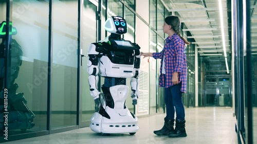 A girl is touching a modern robot while chatting with him photo