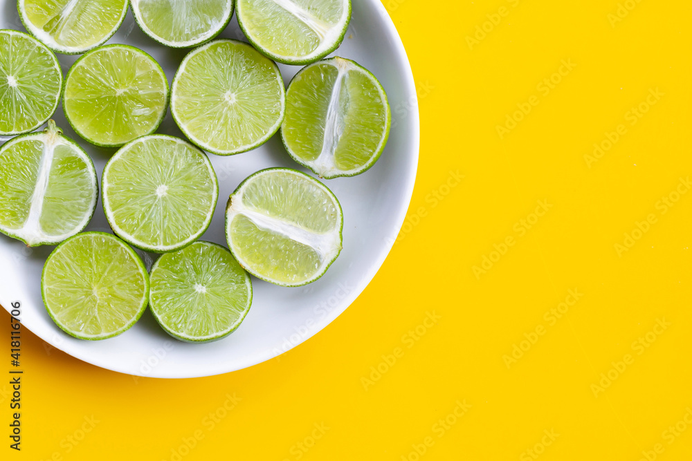 Fresh limes in white dish on yellow background.