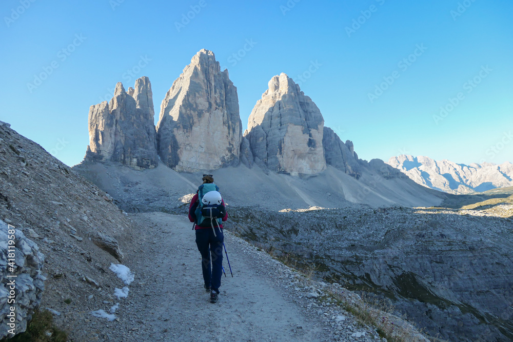 A woman in pink jacket hiking on a gravel road and enjoying the view on the Tre Cime di Lavaredo (Drei Zinnen), mountains in Italian Dolomites. Desolated and raw landscape. Early morning. Daybreak