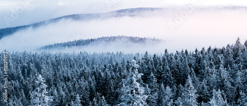 A view from the Orlica observation tower to the mountains with a snow-covered forest and an incoming fog.