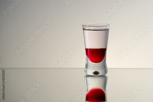 Single, reflected mad dog shot drink with tabasco sauce, raspberry syrup and chilli on side with smooth background