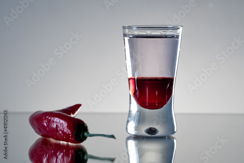 Single, reflected mad dog shot drink with tabasco sauce, raspberry syrup and chilli on side with smooth background