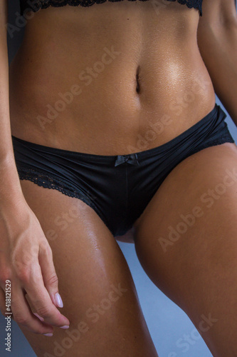 Tanned slim body of a young girl in black underwear on a gray background